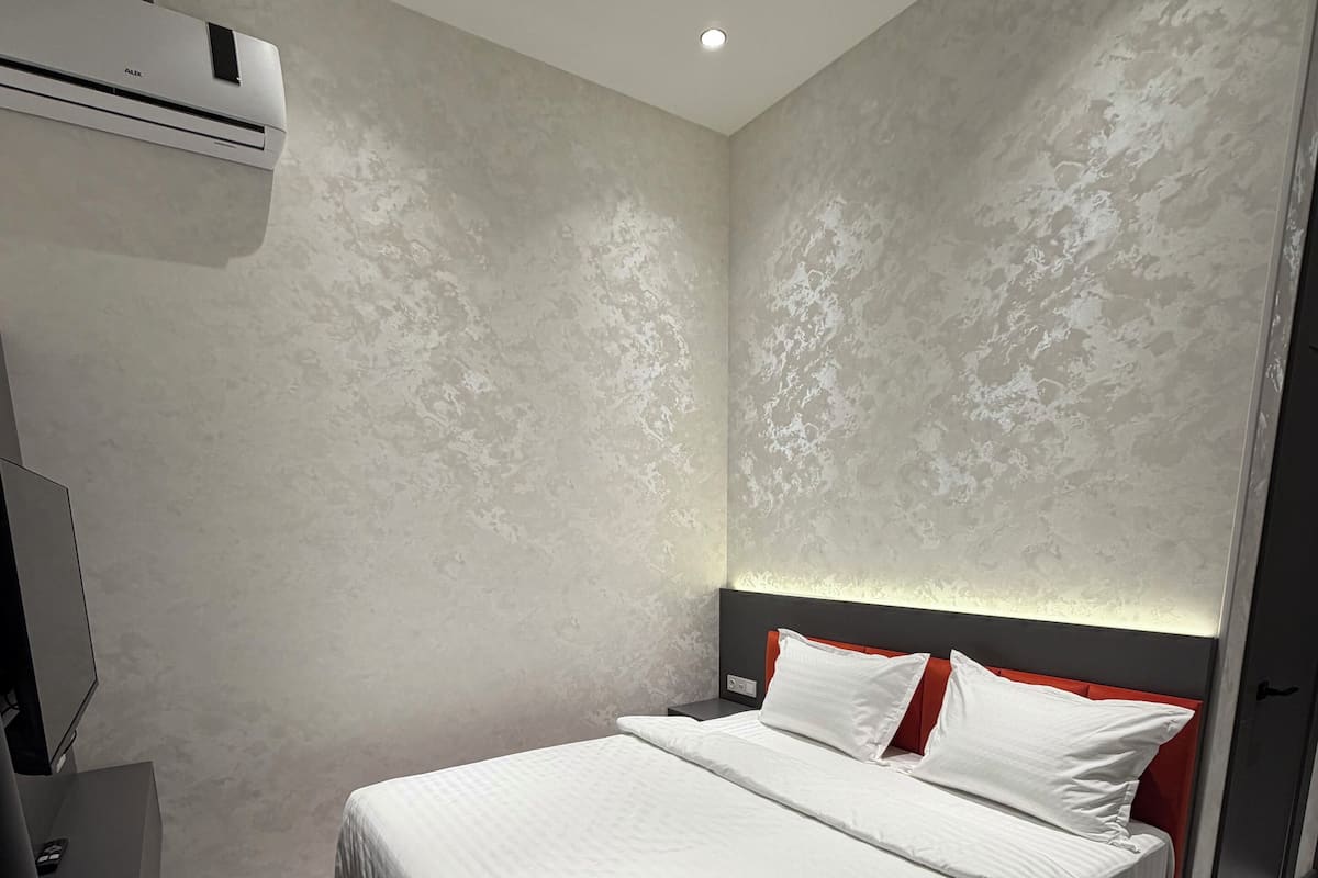 Ein modernes Hotelzimmer mit einem großen Bett, einem Nachttisch, einem Schreibtisch und einer Klimaanlage.