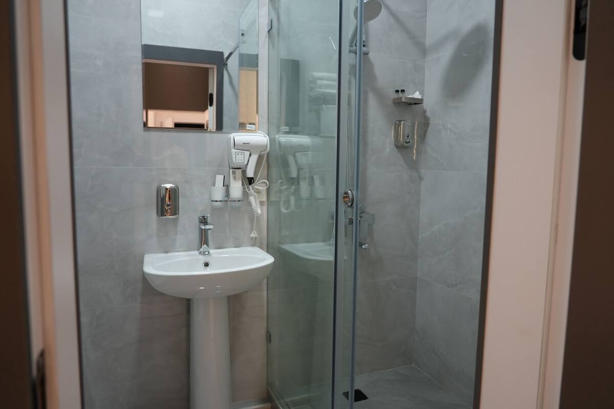 Ein modernes Badezimmer mit einer Duschkabine aus Glas, einem weißen Waschbecken und einem Spiegel darüber.