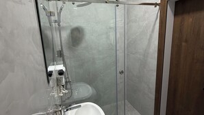 Une salle de bain moderne avec une douche à parois de verre, un lavabo blanc et une porte en bois.