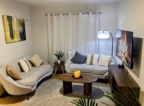 Una sala de estar con dos sofás, una mesa de centro, un televisor y una planta.