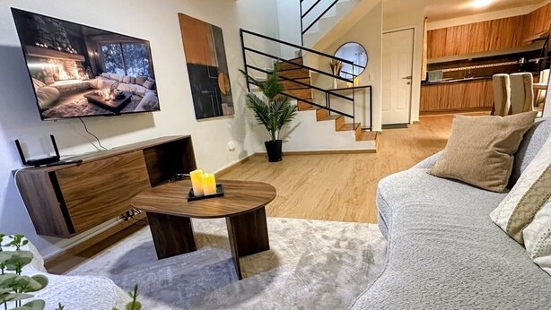 A modern living room with a sofa, a coffee table, a TV, and a staircase leading to a kitchen.