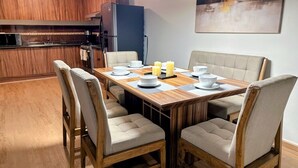 A dining area with a wooden table and chairs, a modern pendant light, and a kitchen in the background.
