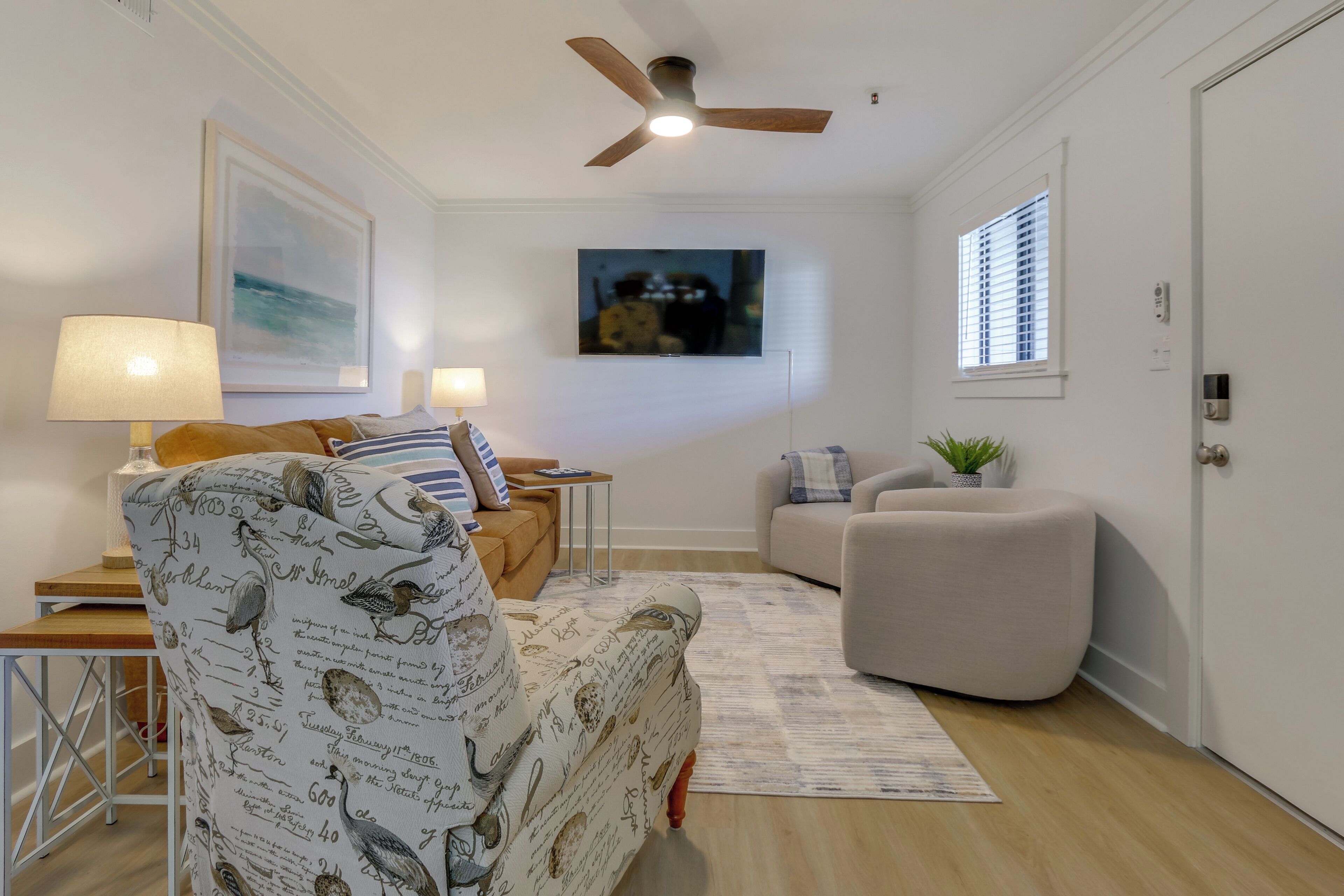 Un salon avec un ventilateur de plafond, un canapé, un fauteuil, une lampe, une table basse et un tapis.