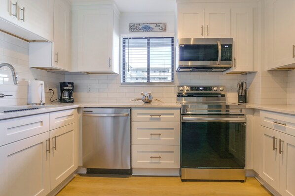 A modern kitchen with white cabinets, stainless steel appliances, and a window with blinds. - Boardwalk to the Beach! Hilton Head Resort Condo (Hilton Head Island)