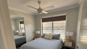 Una camera da letto con un letto, due comodini, una ventola a soffitto, una finestra con tende e una porta.