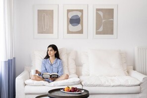 A person sitting on a white sofa with a tray of fruit in front, reading a book. - Lilium Hotel Santorini (Santorini)
