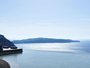 A clear view of a calm sea with a rocky coastline and a distant mountain range. - Lilium Hotel Santorini (Santorini)