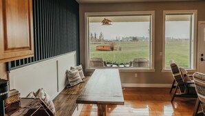 A kitchen with a wooden table, a window with a view of a field, and a ceiling light. - Wheelchair Accessible - Sleeps 10 - Mountain Views - Near Glacier Nat'l Park  (Kalispell)