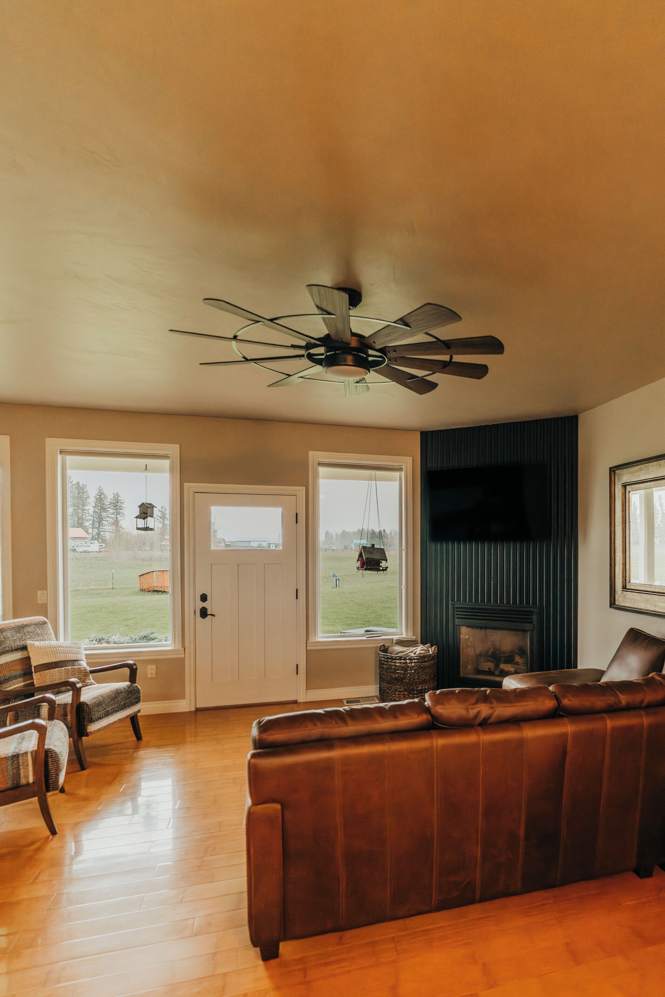 Un salon avec un canapé en cuir marron, un plancher en bois, un ventilateur de plafond et une cheminée.