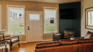 A living room with a brown leather sofa, wooden flooring, a ceiling fan, and a fireplace. - Wheelchair Accessible - Sleeps 10 - Mountain Views - Near Glacier Nat'l Park  (Kalispell)