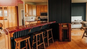 A modern kitchen with wooden cabinets, a bar area with stools, and a large island. - Wheelchair Accessible - Sleeps 10 - Mountain Views - Near Glacier Nat'l Park  (Kalispell)