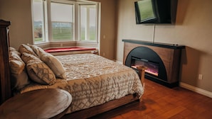 A bedroom with a bed, a fireplace, a television, and a window with a view. - Wheelchair Accessible - Sleeps 10 - Mountain Views - Near Glacier Nat'l Park  (Kalispell)