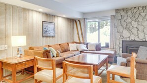 A cozy living room with a wooden panel wall, a stone fireplace, a brown leather sofa, and a wooden coffee table. - 1 Mi to Village & Eagle Lodge: Condo w/ Fireplace (Mammoth Lakes)