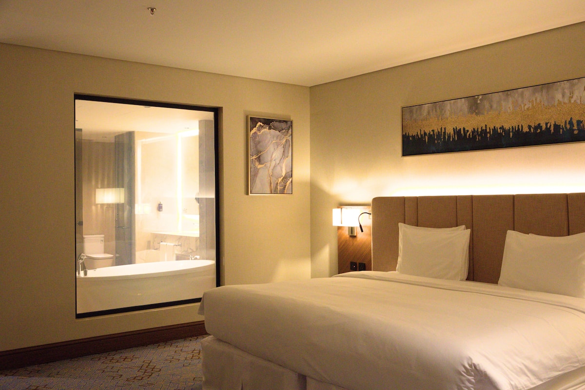 Habitación de hotel con una cama grande, un baño con espejo y un cuadro en la pared.