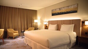 A hotel room with a large bed, two armchairs, a nightstand, and a wall-mounted painting.