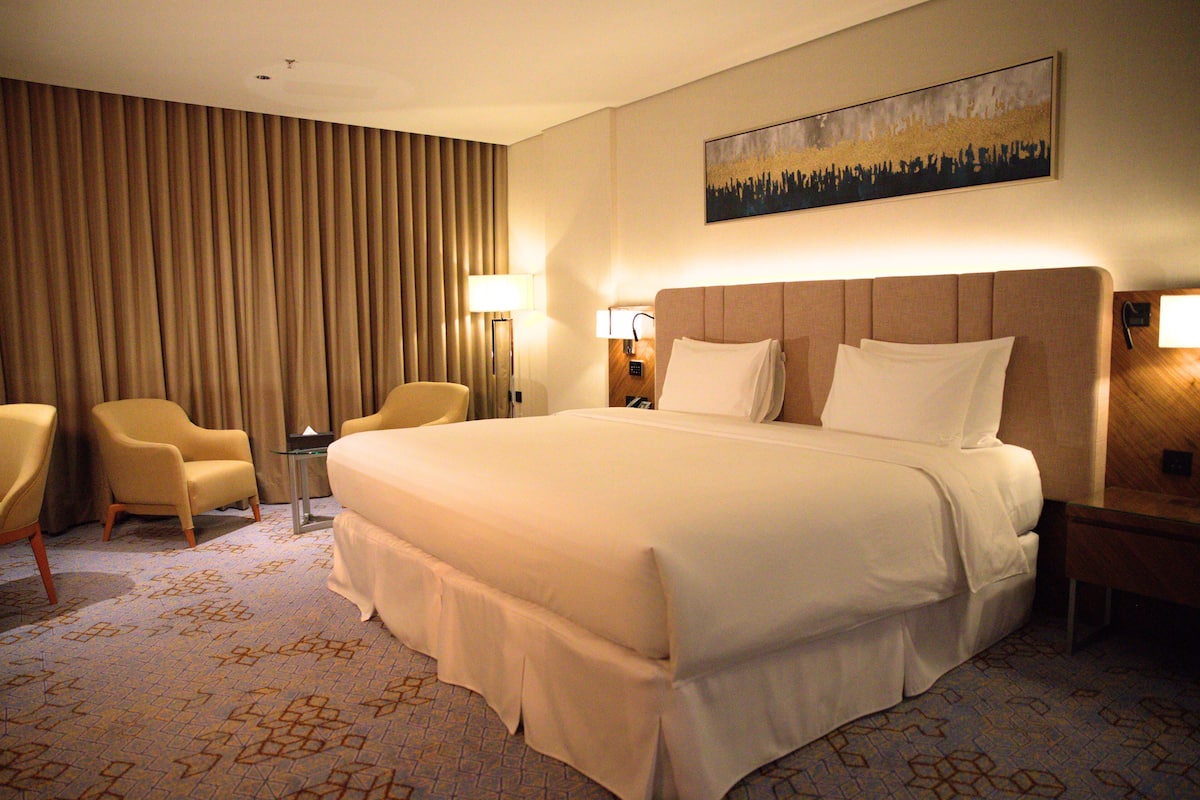 Habitación de hotel con una cama grande, dos sillones, una mesita de noche y un cuadro colgado en la pared.