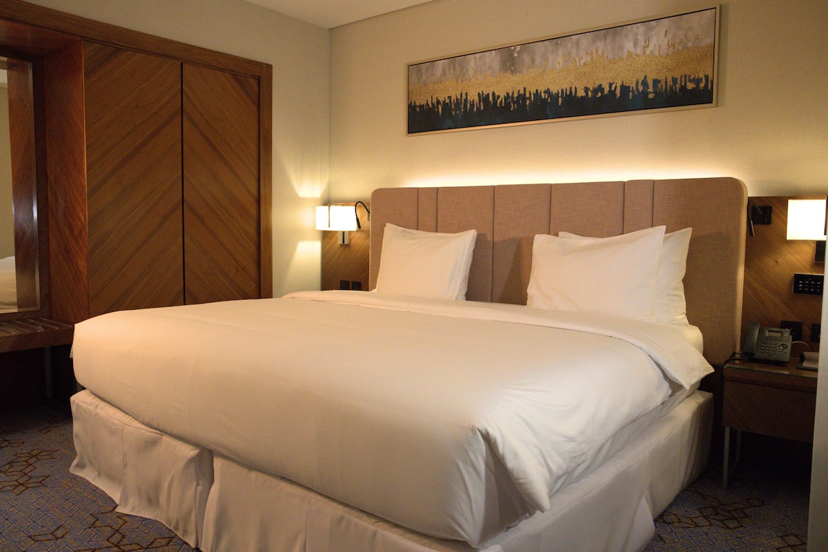 Habitación de hotel con una cama grande, dos lámparas de noche, un armario de madera y un cuadro en la pared.