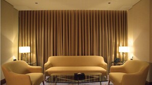 A hotel room with a sofa, two armchairs, a glass coffee table, and a curtain backdrop.