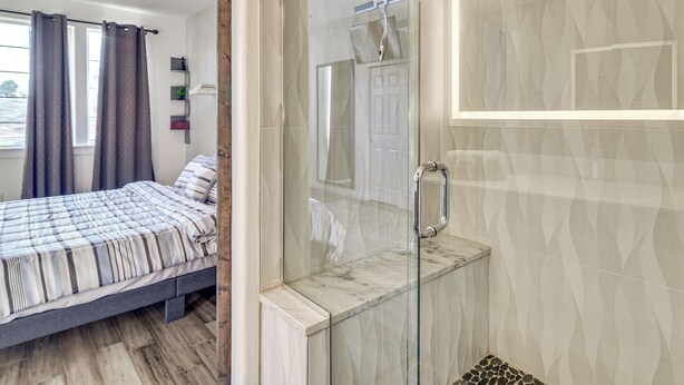 Ein Schlafzimmer mit Bett, Dusche mit Glastüren und Blick ins Freie.