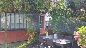 An outdoor patio with a table and chairs, surrounded by lush greenery and a building with large windows. - Accommodation in the Heart of the Nantes Vineyard - Near Clisson (Mouzillon)