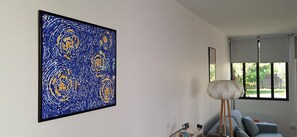 A room with a large abstract painting, a modern lamp, and a view through a window.