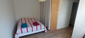 A single bed with striped bedding, a wooden floor, and a white wall.
