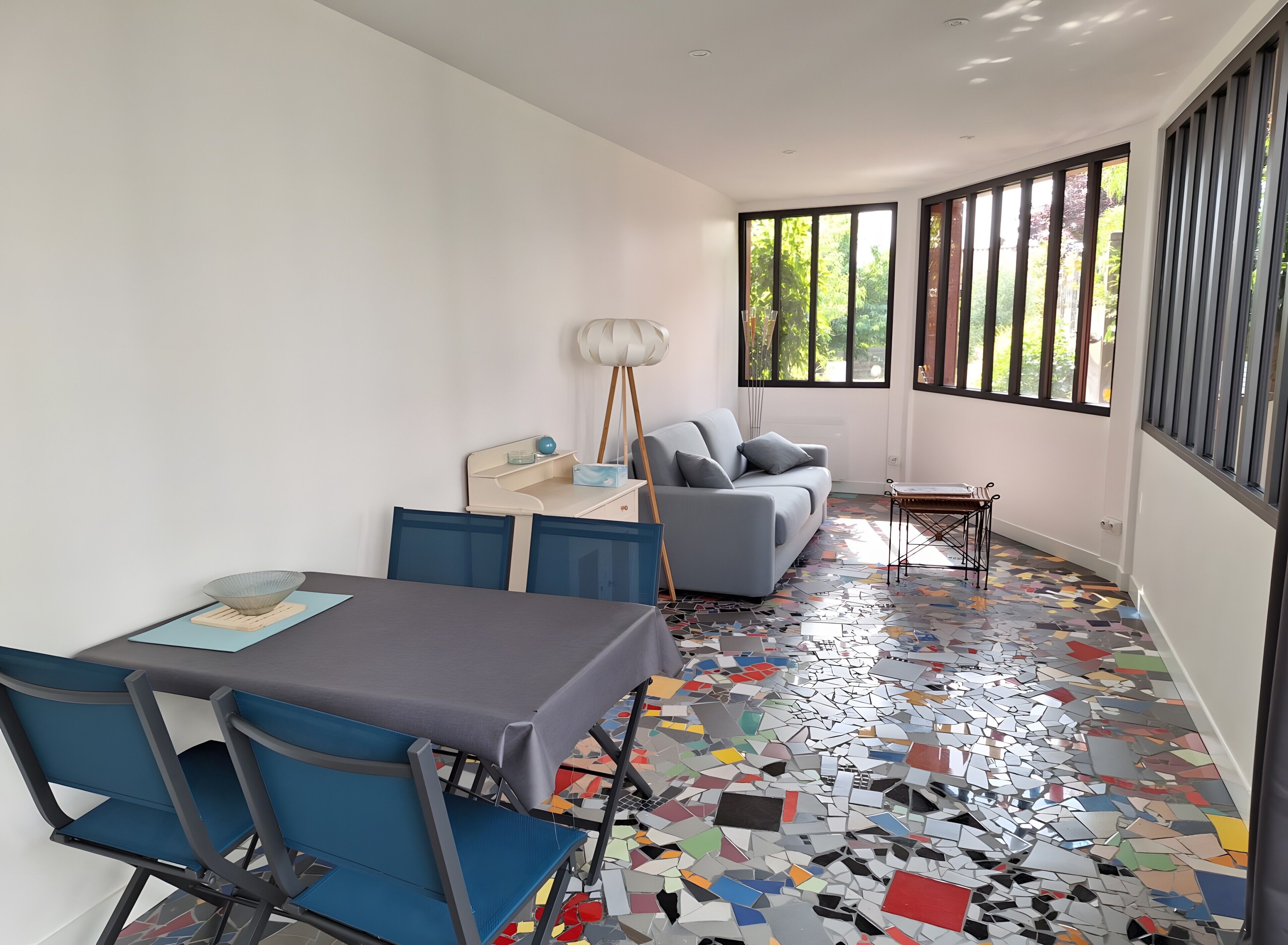 Um interior moderno com uma mesa de jantar, cadeiras, um sofá e um chão com azulejos coloridos e refletivos.