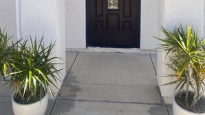 A dark brown door with a decorative design, flanked by two potted plants with green leaves. - Brand-New Modern 2BR /2BA Private Home – Near Little Saigon, K-Town & Disneyland (Santa Ana)