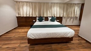 A bedroom with a large bed, wooden flooring, a headboard, and a curtain. - Sindu Executive Lodging (Pune)