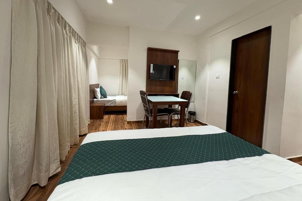 A hotel room with a bed, a desk, a chair, a TV, and a door.