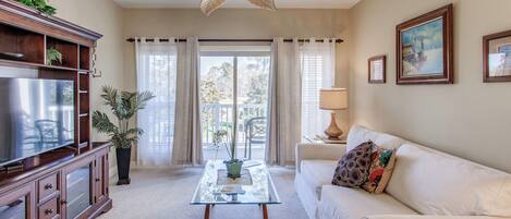A living room with a glass coffee table, white sofa, wooden entertainment center, and a ceiling fan.