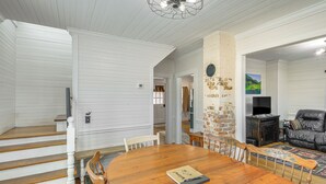 A dining area with a wooden table and chairs, a staircase, a brick wall, and a leather sofa. - Mtn Views, New River Access & 98 Acres: Galax Gem (Galax)