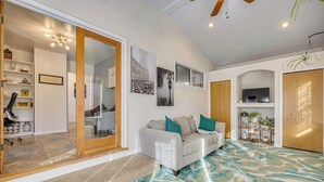 A spacious living room with a large sofa, a coffee table, and a patterned rug. There is a sliding glass door leading to a balcony, and a television mounted on the wall. - 4 Mi to Riverwalk & CSU Pueblo! Home w/ Sunroom (Pueblo)