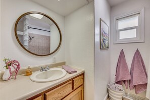 A bathroom with a white sink, wooden vanity, a round mirror, a shower, and two towels hanging on the wall. - 4 Mi to Riverwalk & CSU Pueblo! Home w/ Sunroom (Pueblo)