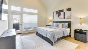 A bedroom with a bed, bedside tables, a desk, and a large window with blinds. - Near NRG Stadium & Med Center | Group Retreat (Houston)
