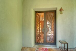 Une porte ornée d’une grille métallique décorative, une petite table et un luminaire fixé au mur.