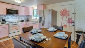 A kitchen with pink cabinets, a stainless steel refrigerator, and a dining table set with bowls and plates. - Hike, Golf & Dine: Tucson Retreat w/ Mtn Views! (Tucson)