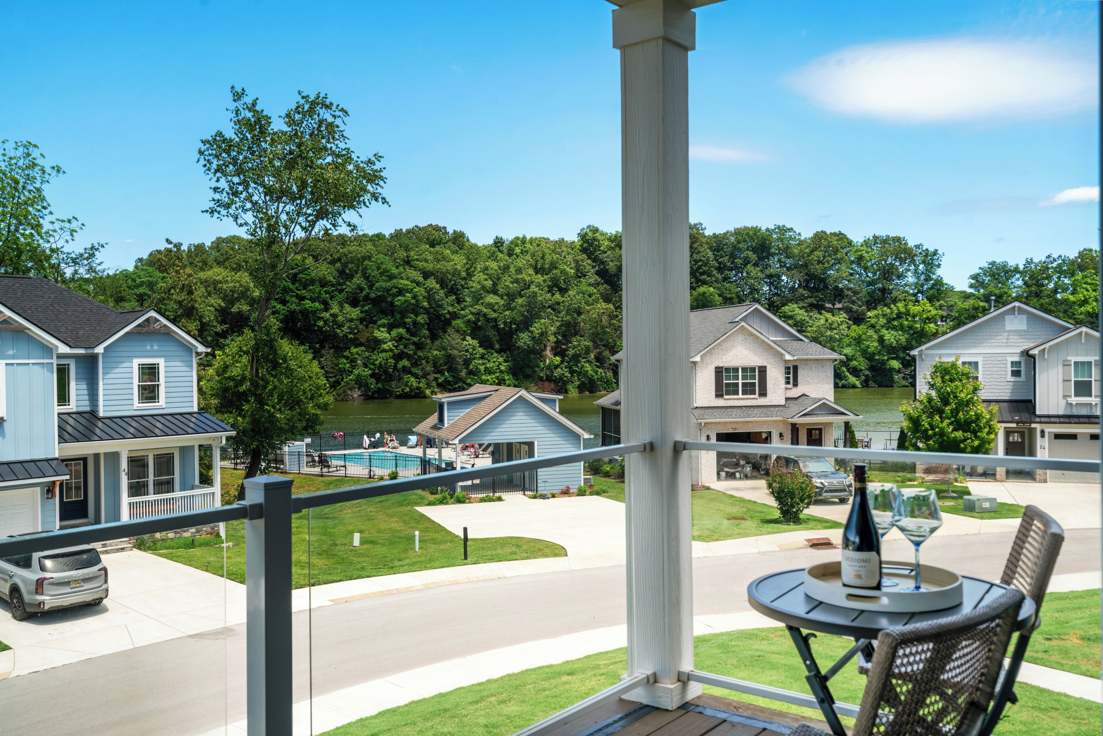A balcony with a table set for two, overlooking a residential area with houses and a swimming pool.