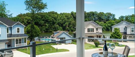 A balcony with a table set for two, overlooking a residential area with houses and a swimming pool.