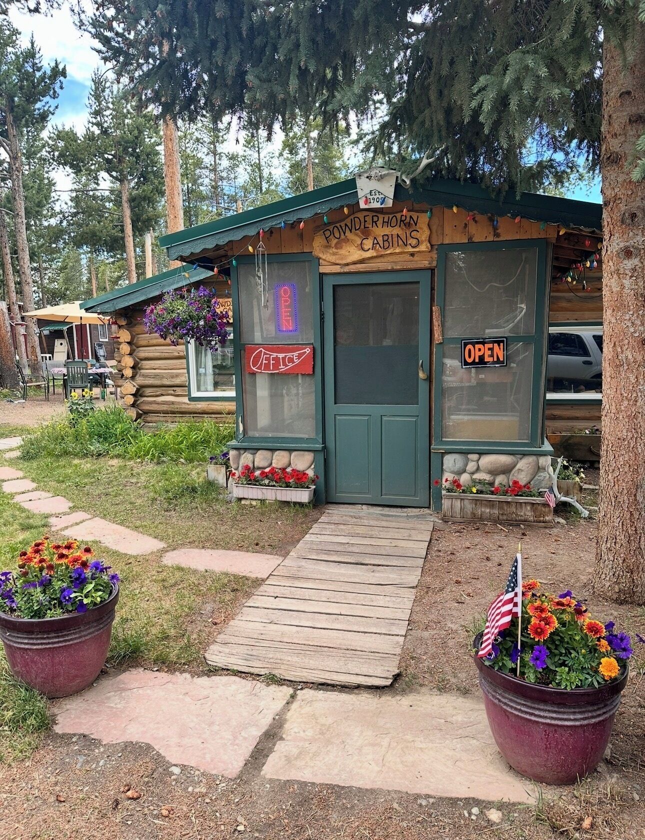 A rustic log cabin with a sign reading "Powderhorn Cabins Office" and an "OPEN" sign on the door.