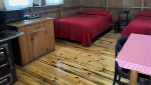Ein rustikales Ferienhaus-Interieur mit Holzboden, einer Küchenzeile, einem Bett mit roter Bettwäsche und einem Tisch mit rosa Tischdecke.