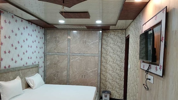 A bedroom with a bed, a TV mounted on the wall, and a small stool. - Hotel Tulsi Palace (Jaipur)