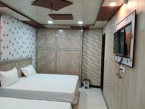 Un dormitorio con cama, televisor montado en la pared y un taburete pequeño.