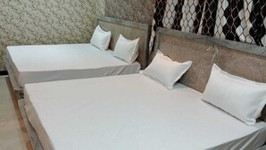 Two single beds with wooden headboards and white bedding in a room with patterned wallpaper. - Hotel Tulsi Palace (Jaipur)