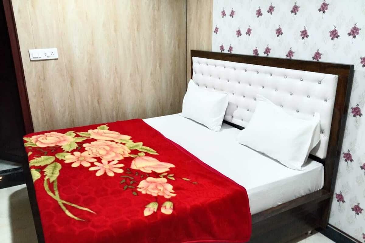 Un lit avec une couvre-lit à motifs floraux rouges, des oreillers blancs et une tête de lit en bois.