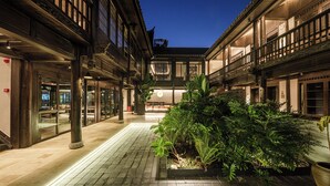Un patio con una zona de estar central, rodeado de edificios de arquitectura tradicional y un sendero bien iluminado.