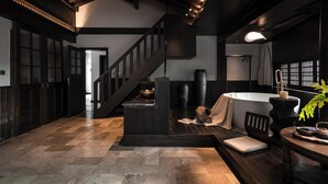 Una habitación amplia con suelo de madera, un ventanal grande, una chimenea y una escalera que sube a un nivel superior.
