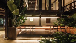Un espacio interior amplio con un mostrador de recepción de madera, plantas en macetas grandes y un techo con vigas a la vista y una lámpara circular.