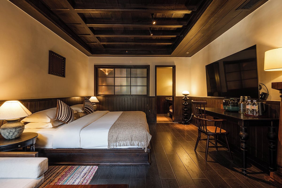 Quarto de hotel com uma cama grande, área de estar com mesa e cadeiras, espaço bar com garrafas e uma televisão.