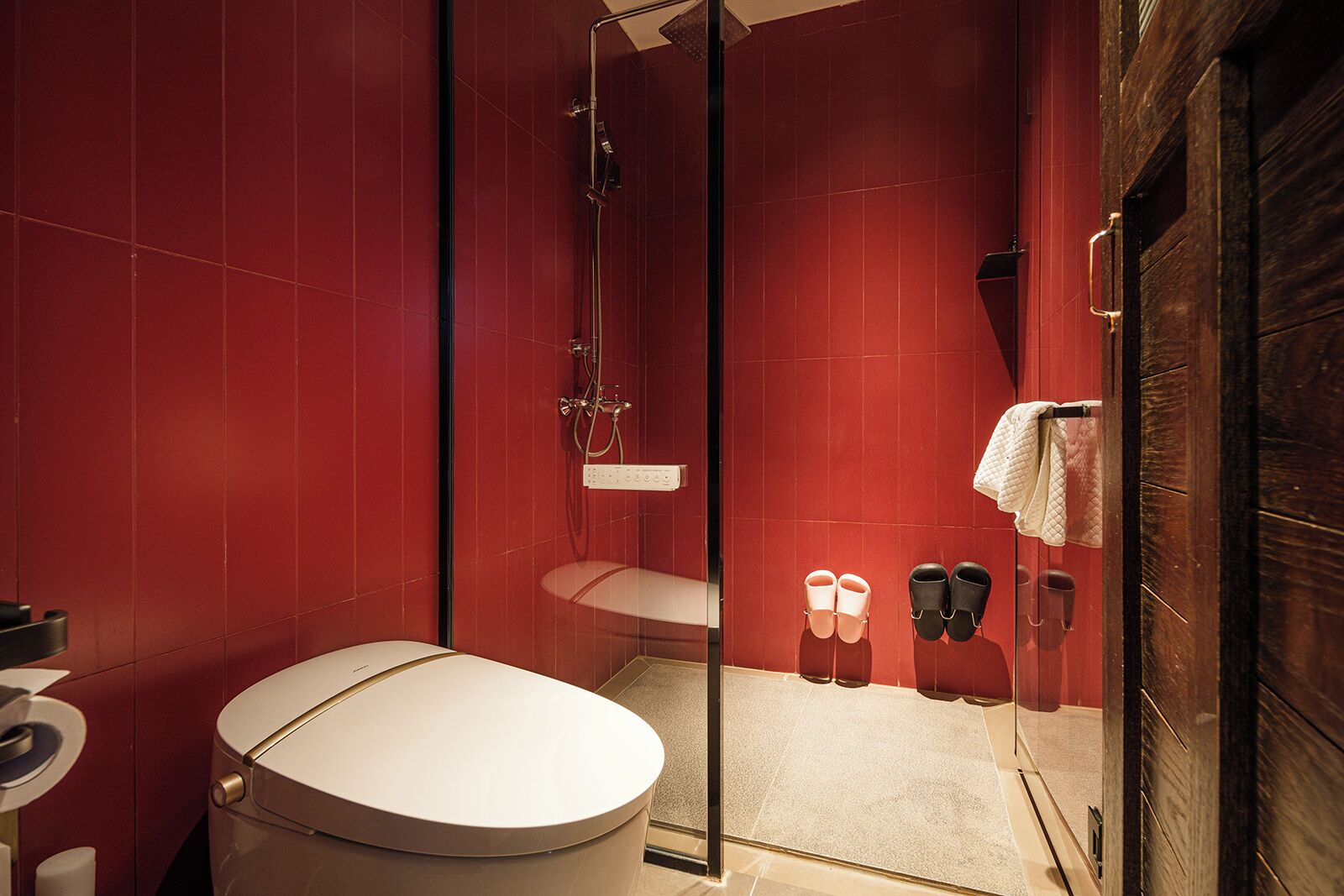 A modern bathroom with red tiles, a glass-enclosed shower, a toilet, and a sink.